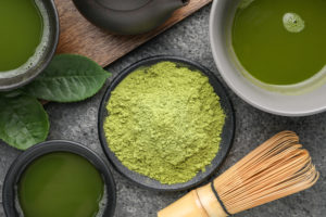 Ciotolina di polvere di tè matcha, accanto a due ciotole di tè con frusta