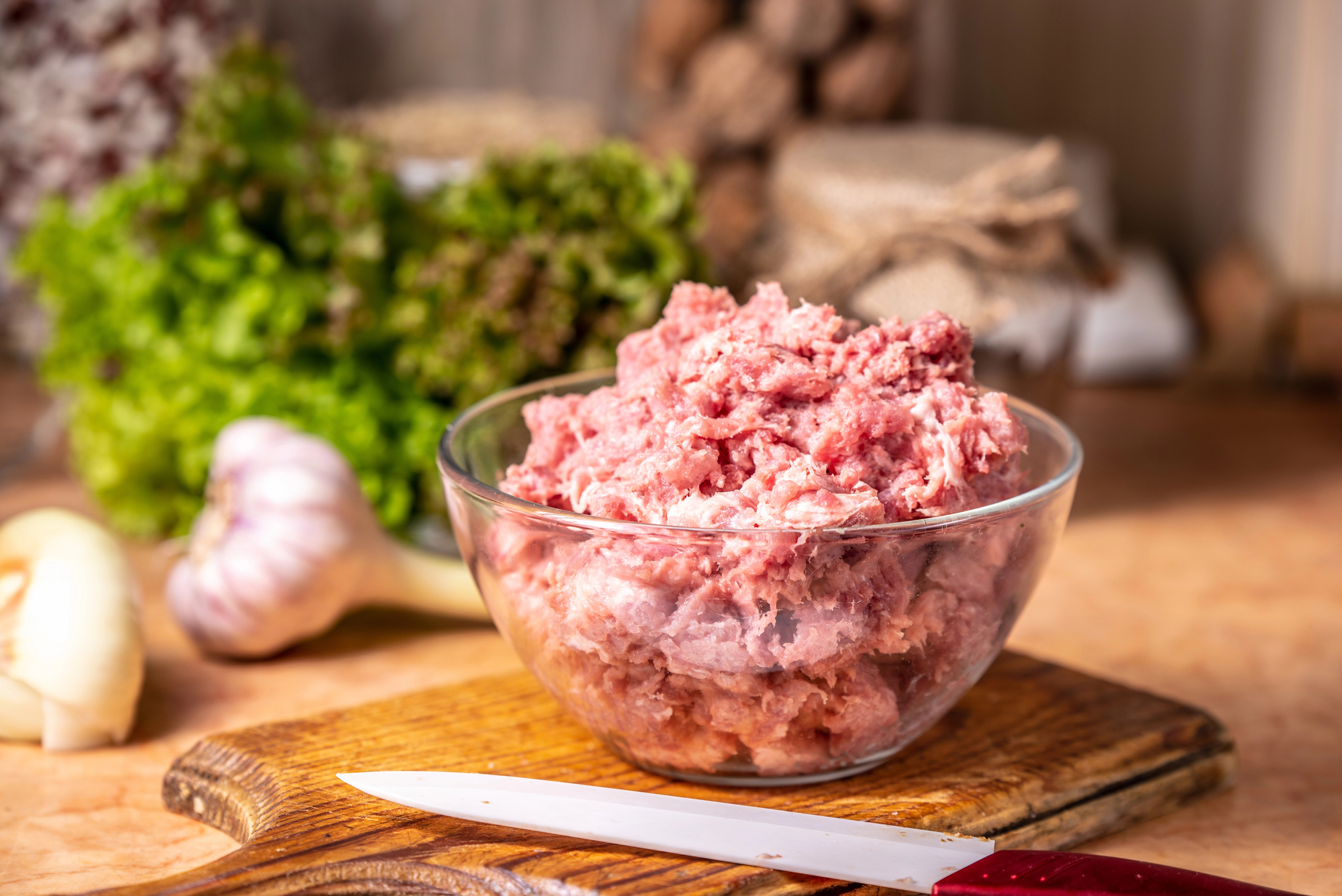 Carne macinata di maiale in una ciotola di vetro su un tagliere di legno accanto a un coltello