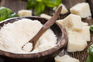 Formaggio Grana Padano o Parmigiano reggiano grattugiato in una ciotola accanto a pezzi di formaggio