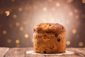 Panettone appoggiato su un centrino su un tavolo di legno, sullo sfondo lucine sfuocate; concept: dolce di Natale, zuccheri, feste, panettoni