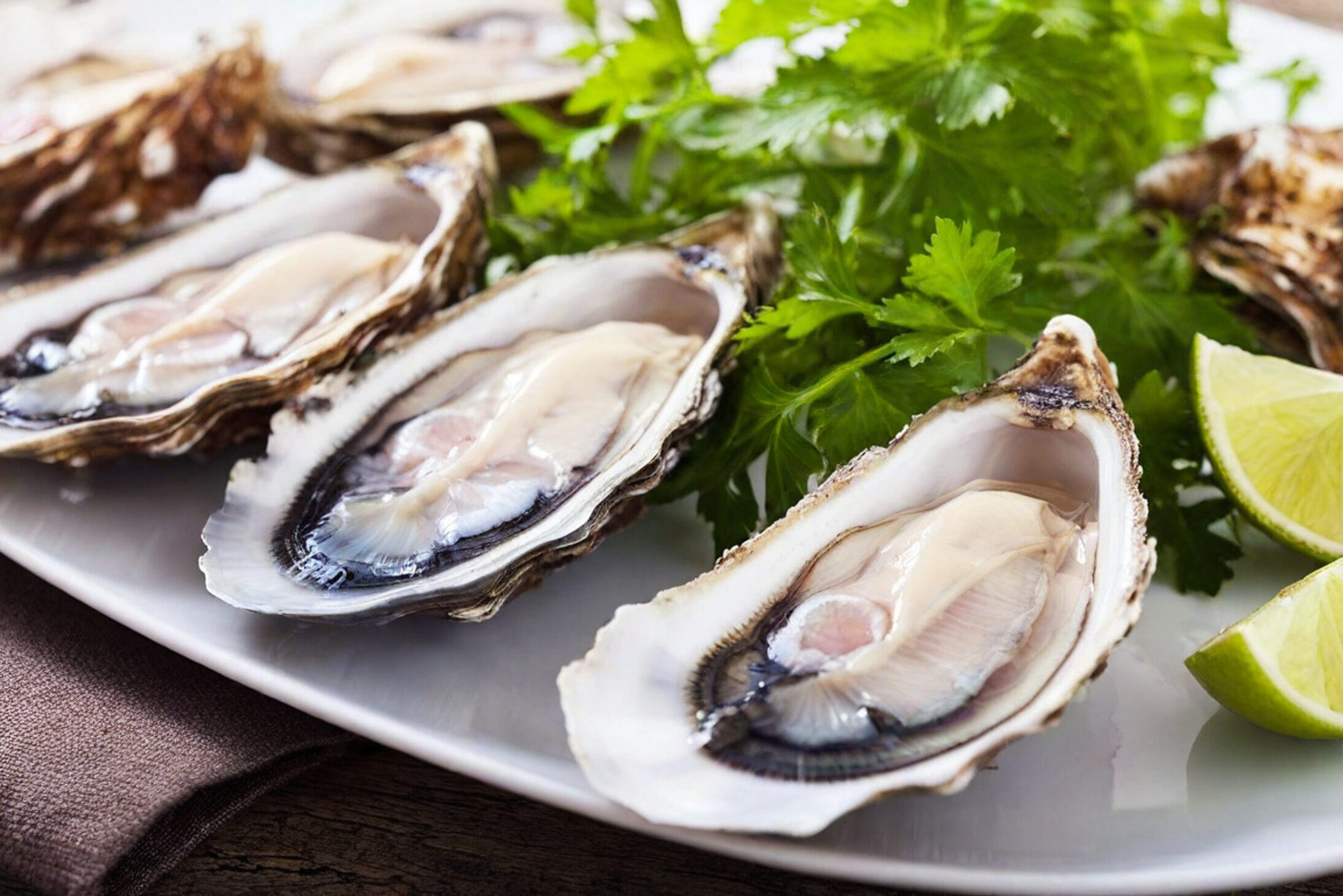 Ostriche crude aperte su un piatto con prezzemolo e fette di lime