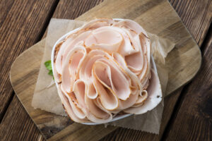 Affettato di petto di pollo o tacchino al forno disposto in una ciotolina su un tagliere di legno