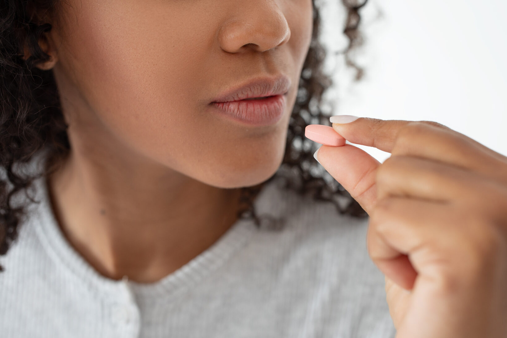 Un primo piano cattura un momento in cui una giovane donna con i capelli ricci sta per ingerire una piccola pillola, evidenziando l'importanza della salute e dell'aderenza quotidiana ai farmaci, ritagliato pastiglia pillola farmaci medicine integratori pills acqua