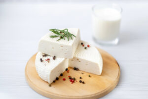 Forma di formaggio fresco tipo primosale o primo sale su un piattino di legno con grani di pepe e rosmarino, sullo sfondo bicchiere di latte