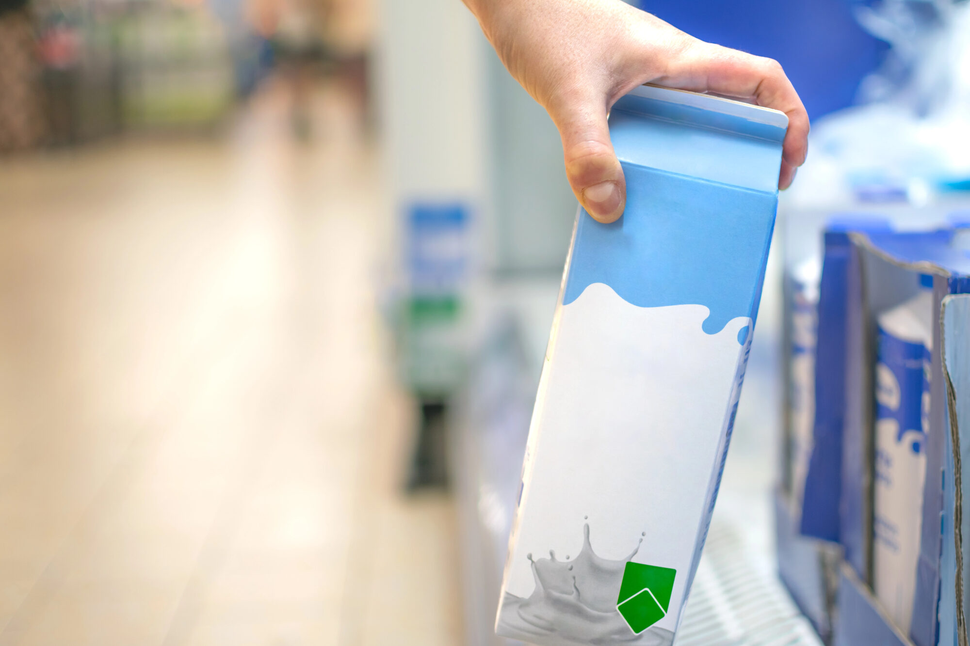 Mano prende un cartone di latte dallo scaffale di un supermercato