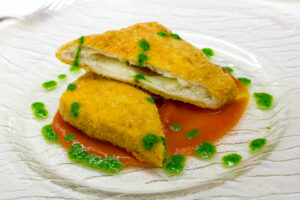 Mozzarella in carrozza tagliata a metà in obliquo, su un piatto con salsa al pomodoro e salsa verde