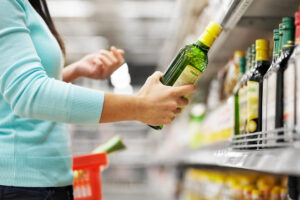 Una donna prende una bottiglia di olio extravergine di oliva dallo scaffale di un supermercato