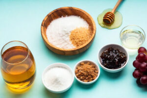 Ingredienti zuccherini assortiti in varie ciotole di legno, ceramica e vetro: zucchero bianco, zucchero di canna, sciroppi vari tipo agave e acero, miele