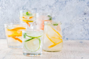 Cocktail estivi sani, set di varie acque infuse di agrumi, limonate o mojito, con lime limone arancia pompelmo, bevande dietetiche detox, in diversi bicchieri sfondo chiaro spazio di copia acqua acque aromatizzate estate idratazione fresco