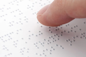 Un dito scorre su una scritta in braille; concept: disabili, disabilità, persone cieche, ipovedenti
