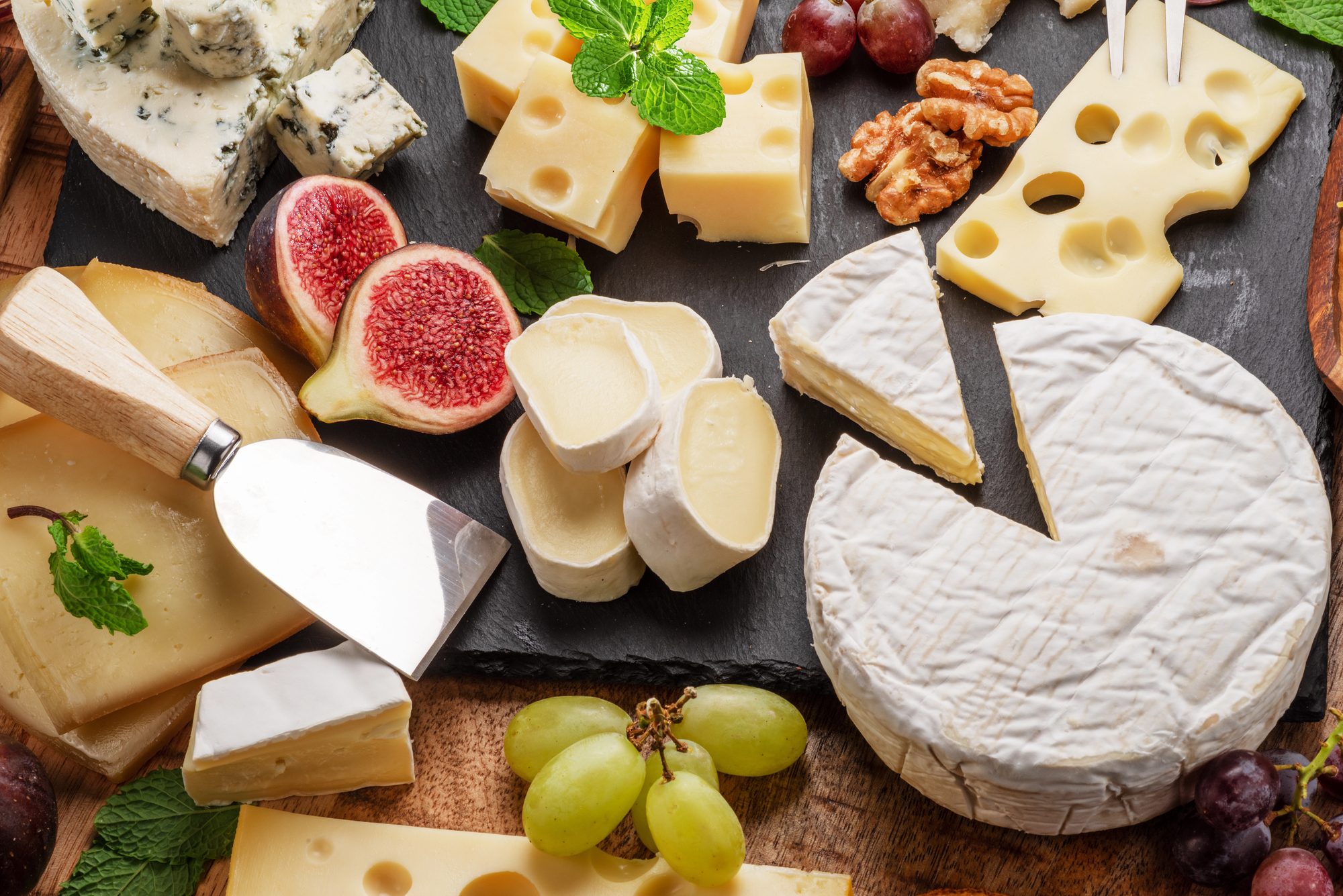 Tagliere di formaggi assortiti con fichi, uva e foglie di menta