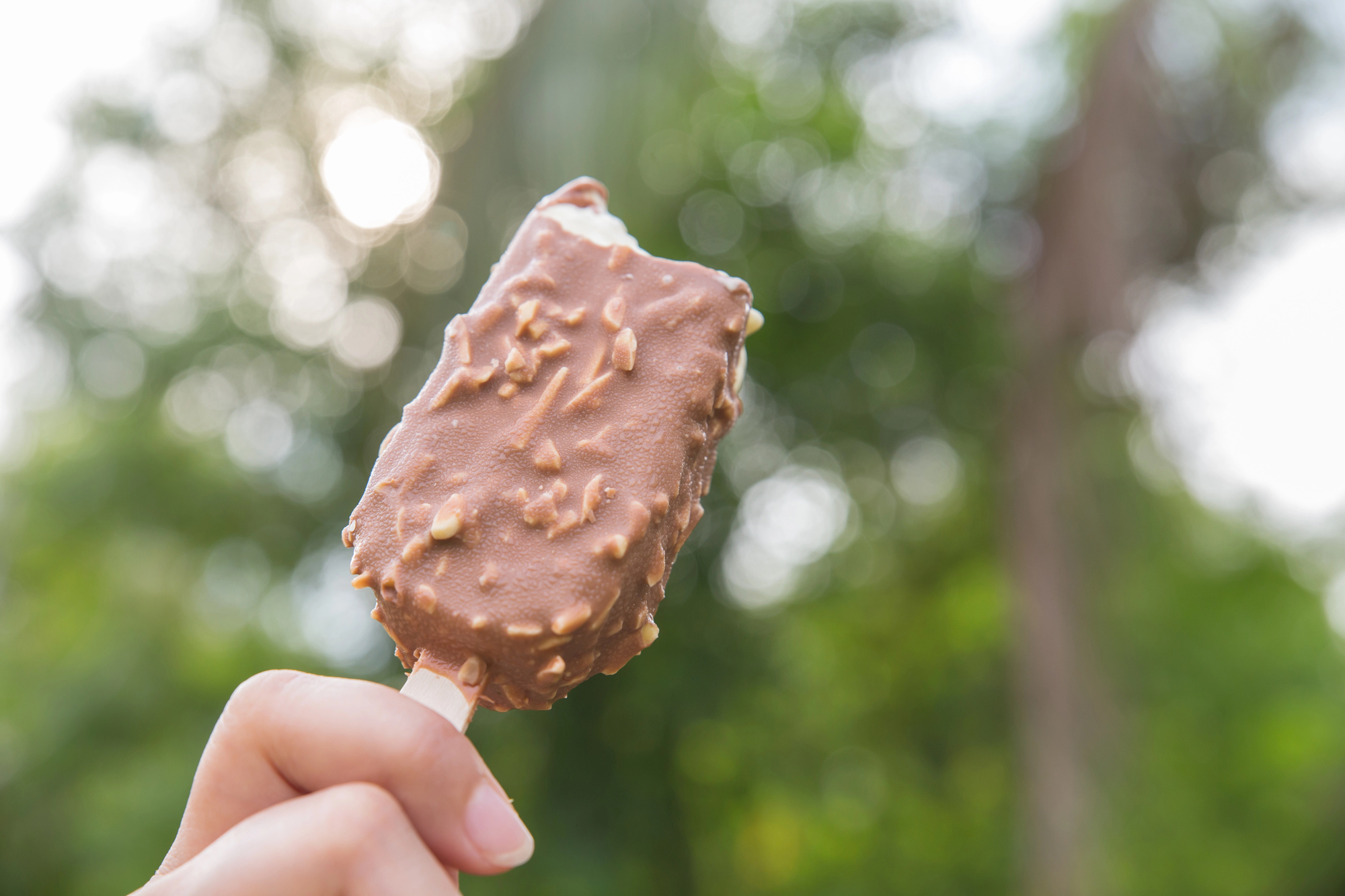 Una persona tiene in mano un gelato industriale su stecco ricoperto di cioccolato e mandorle