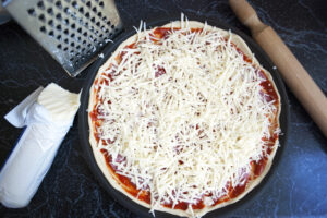 Pizza appena preparata, ancora da infornare, con mozzarella per pizza grattugiata