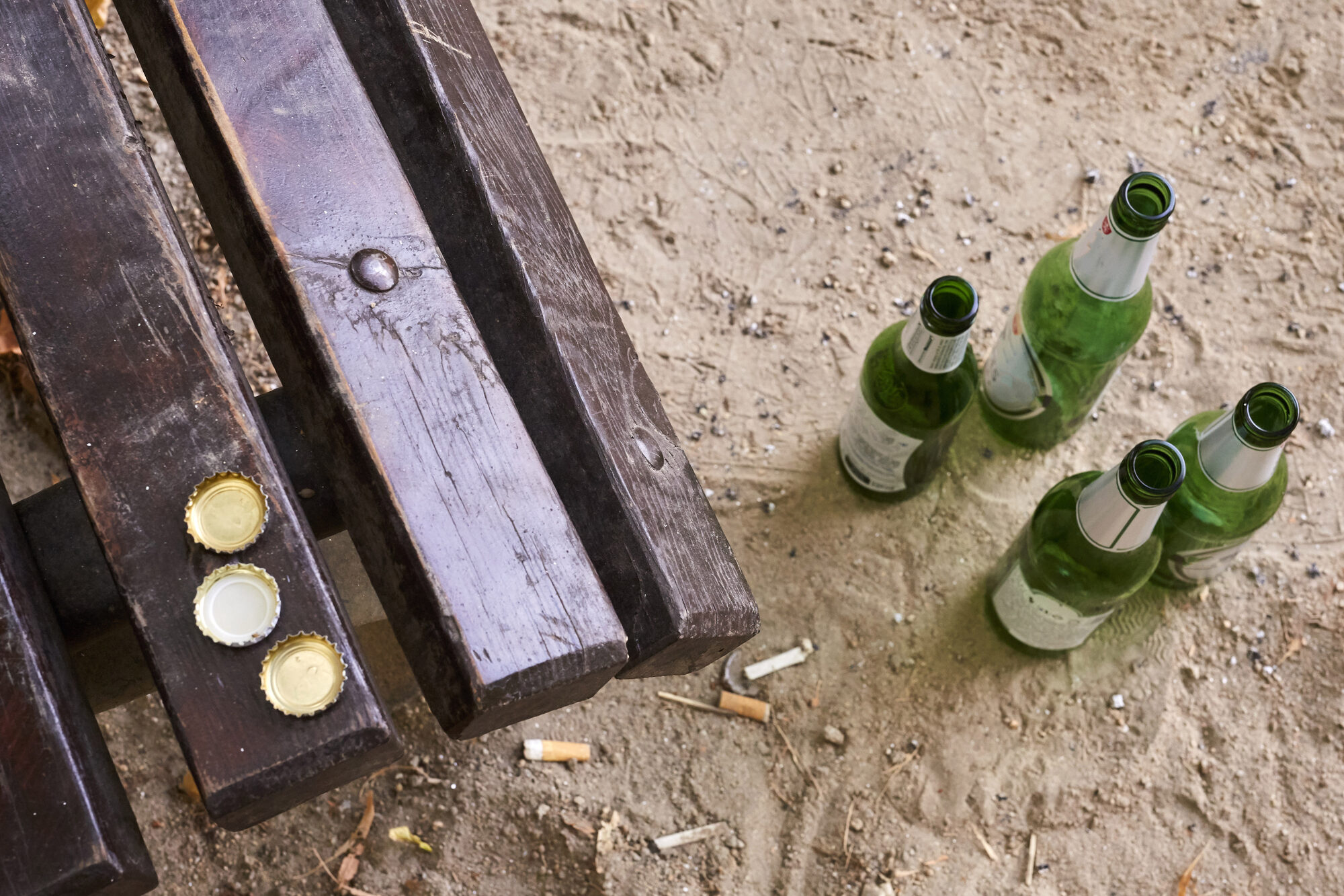 Quattro bottiglie di birra in vetro abbandonate vicino alla panchina di un parco; concept: rifiuti, vuoto a rendreå