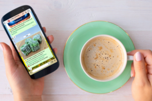 Una donna tiene con una mano il manico di una tazza di cappuccino e con l'altra uno smartphone; concept: Servizio alert, canale Whatsapp, allerte e richiami