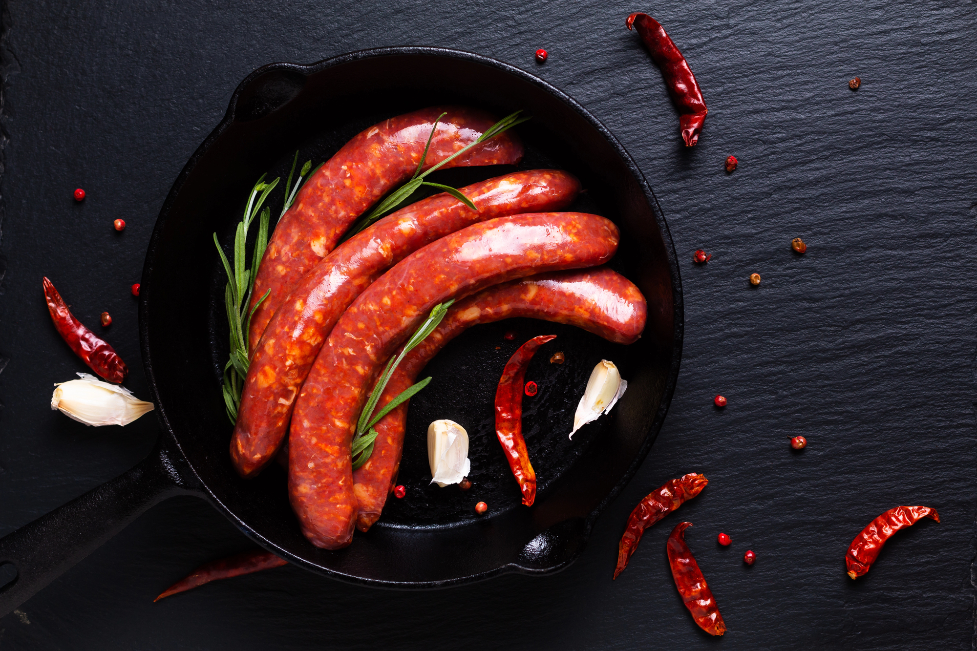 Salsicce crude piccanti in una padella di ghisa con aglio peperoncino e rosmarino; concept: salsiccia