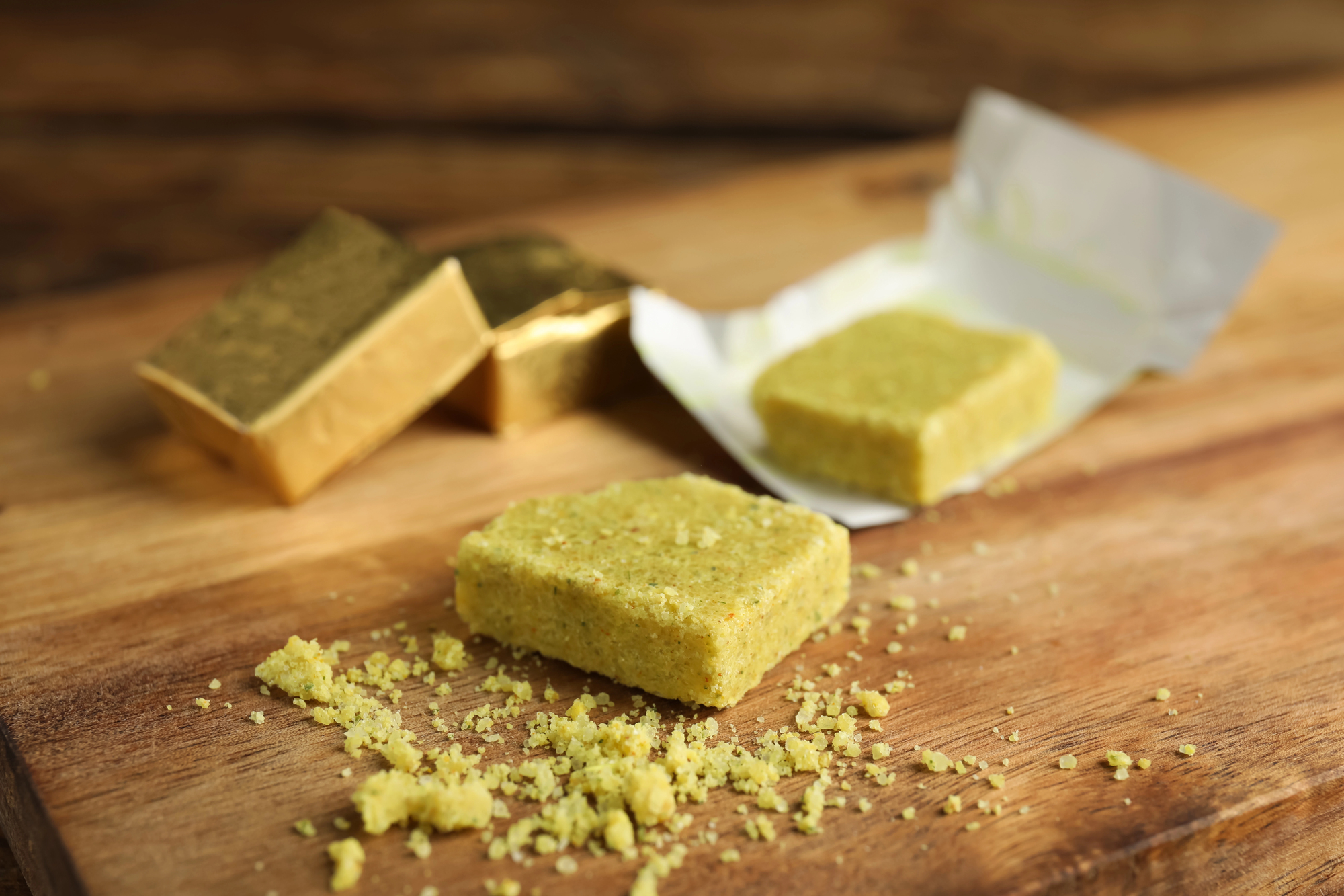 Alcuni dadi da brodo incartati e scartati su un tagliere di legno