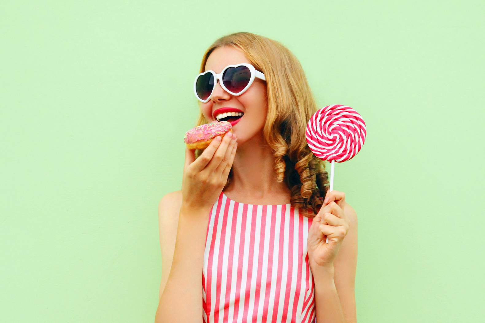 donut junk food dessert dolci zuccheri zucchero ragazza che mangia una ciambella mentre tiene in mano un lecca-lecca su uno sfondo verde