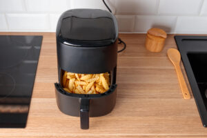 Friggitrice ad aria con patatine fritte nel cestello sul piano di lavoro di una cucina, tra piastra a induzione e lavandino